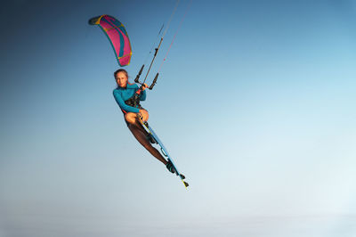 Caucasian woman kitesurfer athlete doing a trick in the air against a blue sky without a cloud