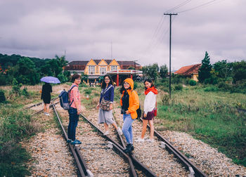 Portrait of female friends standing on railroad tracks against cloudy sky
