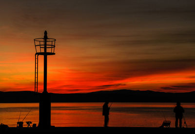 Silhouette people on calm lake at sunset