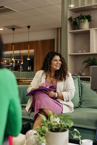 Smiling female business professional sitting with file on sofa at office