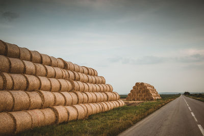 Stack of road by agricultural field against sky