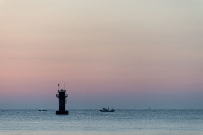 Lighthouse on sea against sky during sunset