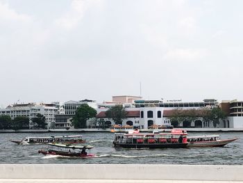 Boats sailing in river against sky in city