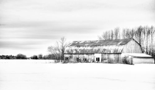 Snow covered field by houses against sky