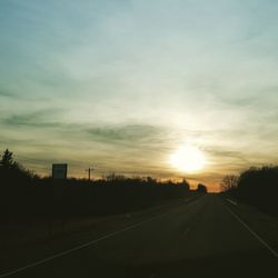 Road amidst silhouette trees against sky during sunset