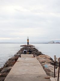 Lighthouse on pier by sea against sky