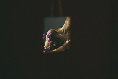 Midsection of woman with flowers against black background