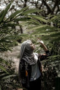 Woman wearing hijab standing by plants