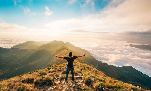 Rear view of man standing on mountain against sky