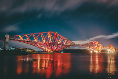 Illuminated bridge over river against sky at night