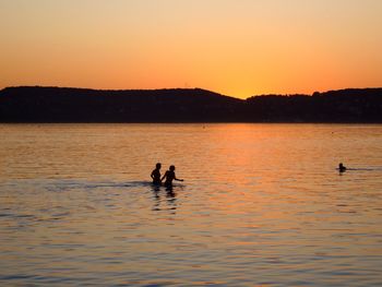 Silhouette man swimming in lake against sky during sunset