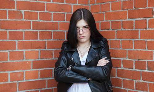 Portrait of a beautiful young woman standing against brick wall