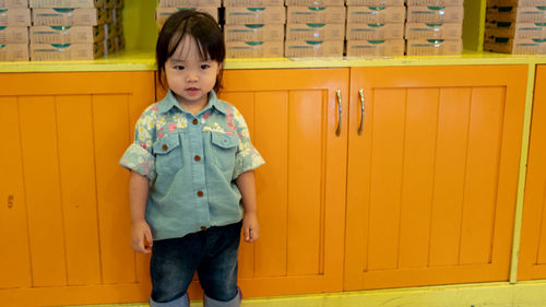 Portrait of cute girl standing against cabinet