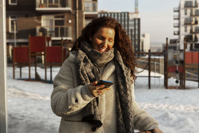 Young woman using mobile phone in city during winter