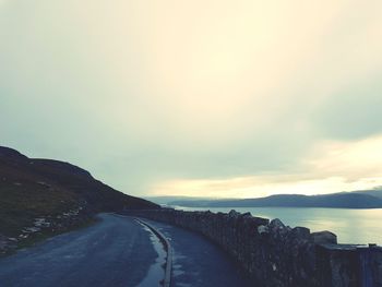 Road by mountains against sky during sunset