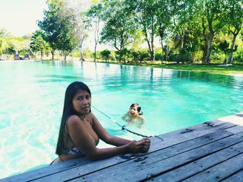 Portrait of woman sitting in swimming pool against trees