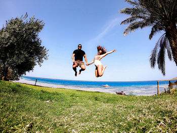 Playful couple jumping at beach against sky