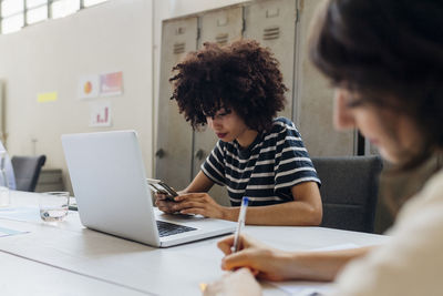 Businesswoman with laptop using smart phone at office