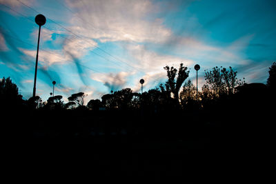 Silhouette of trees on landscape against cloudy sky