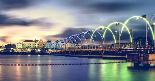 Illuminated bridge over river against cloudy sky