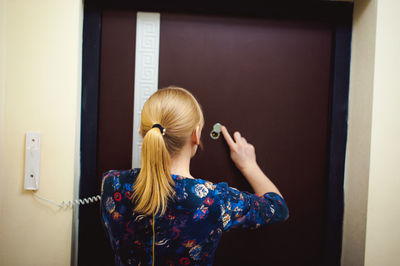 Rear view of woman talking on telephone while standing against door