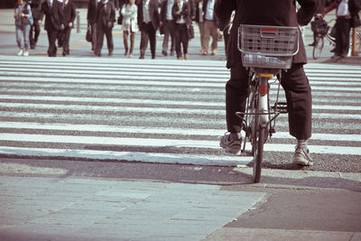 Low section of man cycling while business people walking on road