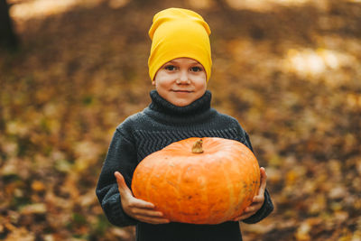 Happy funny little boy teen child in a hat holding a big pumpkin is getting ready for halloween