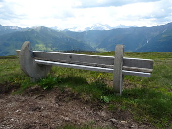 Bench on field by mountains against sky