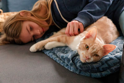 A young adolescent girl lying on a couch finds comfort by snuggling and petting her tabby cat