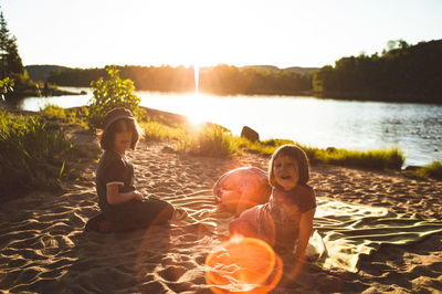 Playful children by lake against sky late in the day