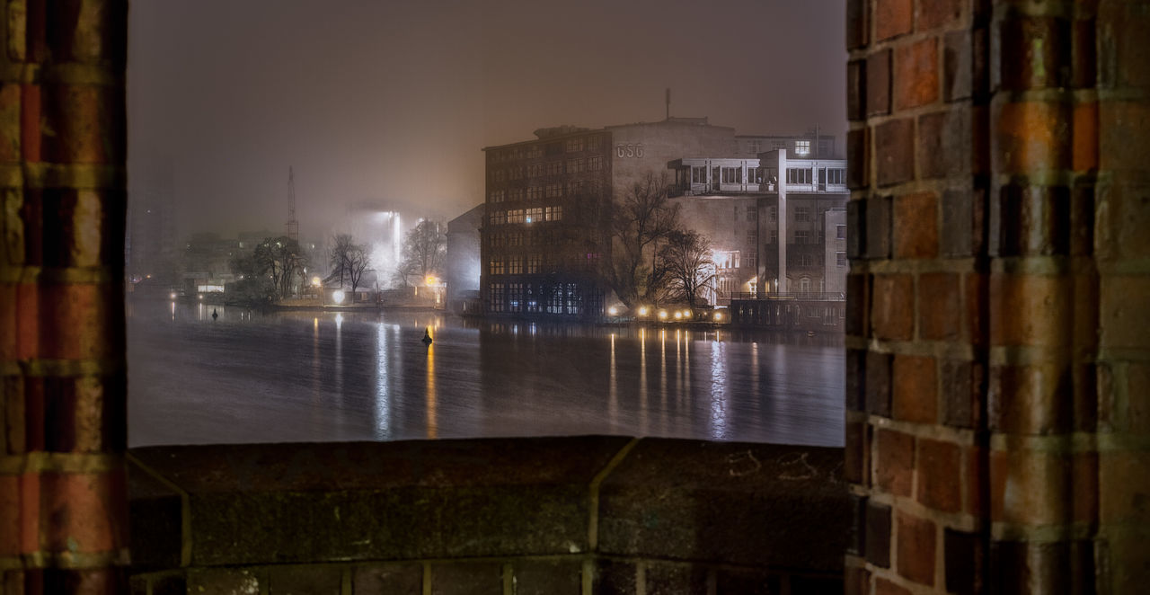 ILLUMINATED BUILDINGS SEEN THROUGH WET GLASS WINDOW