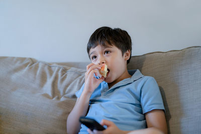 Portrait of boy looking away while sitting on sofa at home