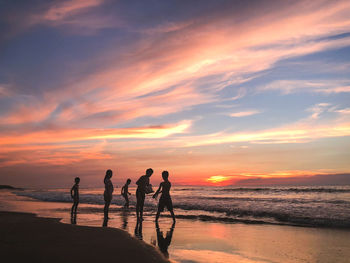 Silhouette people on beach against sky during sunset