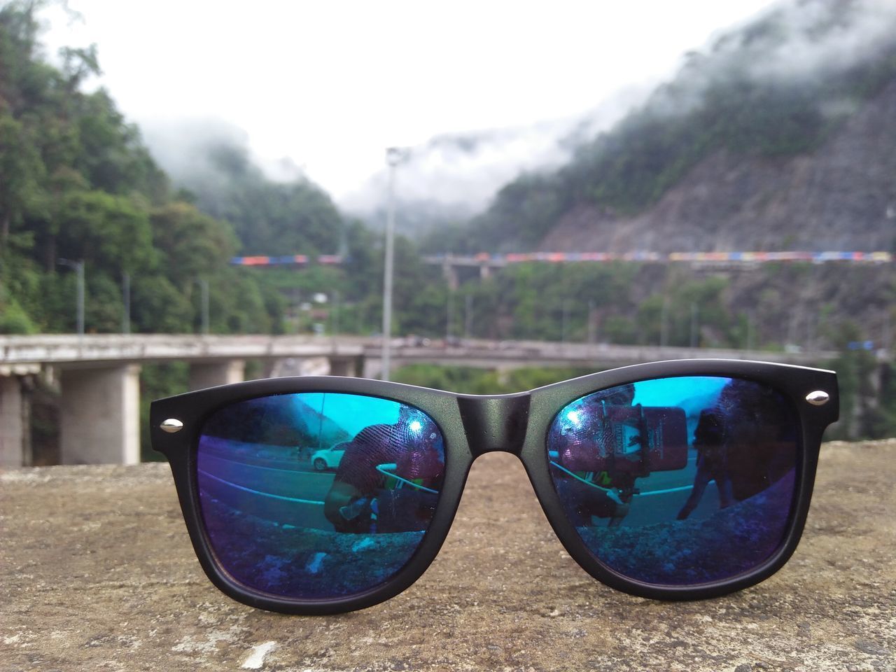 CLOSE-UP OF SUNGLASSES ON SIDE-VIEW MIRROR AGAINST TREES