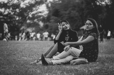 Young women sitting on grass against trees