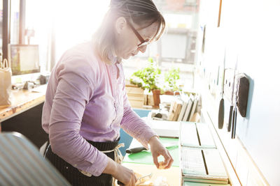 Side view of female owner cutting cheese in store