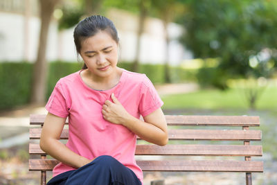 Young woman suffering from chest pain while sitting on bench at park