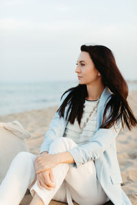 Beautiful young woman sitting on beach against sea