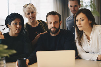 Business colleagues using laptop at conference table together in board room