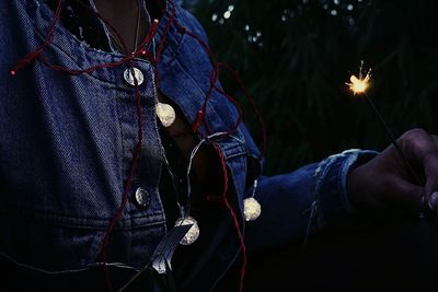 Midsection of person holding illuminated sparkler at night