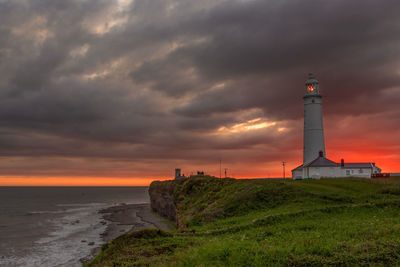 Lighthouse by sea against sky during sunset