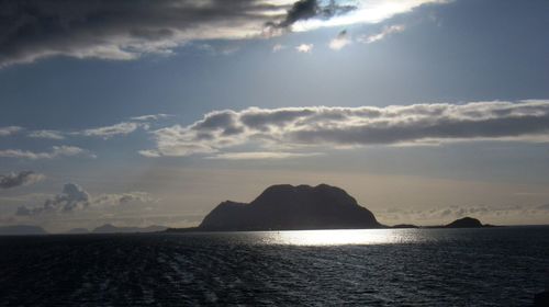 Scenic view of sea by mountain against sky