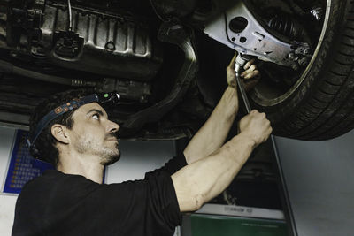 Mechanic with head flashlight using ratchet to adjust detail of car wheel while working in garage