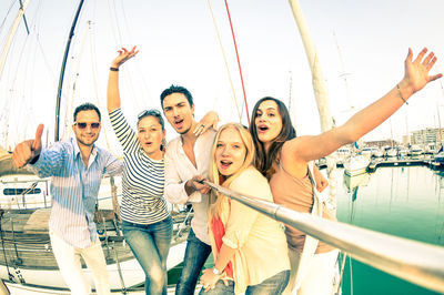 Portrait of happy friends standing at harbor against clear sky