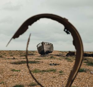 Abandoned boat on beach against sky through rusty metal frame