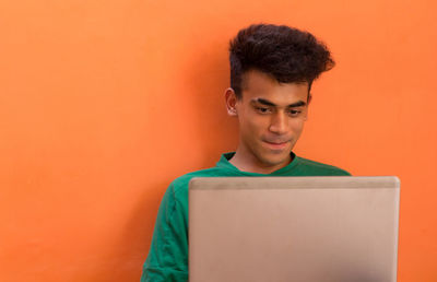 Portrait of mature man using mobile phone against orange wall