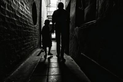 Rear view of father and son walking at alley amidst houses