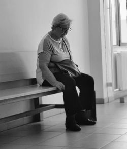 Full length of woman sitting on bench against wall