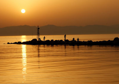 Silhouette people fishing on pier amidst sea against sky during sunset