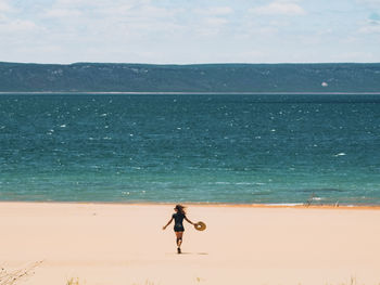 Rear view of woman walking at beach against sky